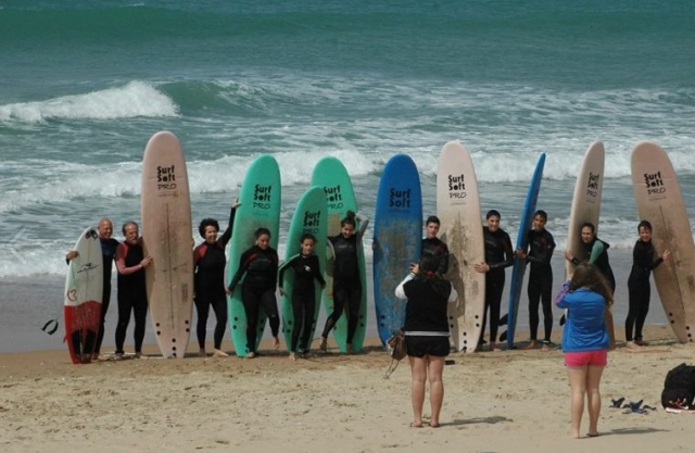 grupo de chicos con sus monitores junto a unas tablas de surf en la playa